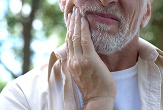 Man in need of dental implant salvage in McKinney puting hand on cheek