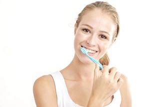 Woman in white shirt brushing teeth against light background