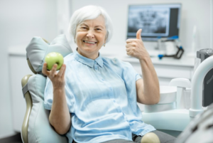 Senior woman holding an apple and gesturing with a thumbs-up